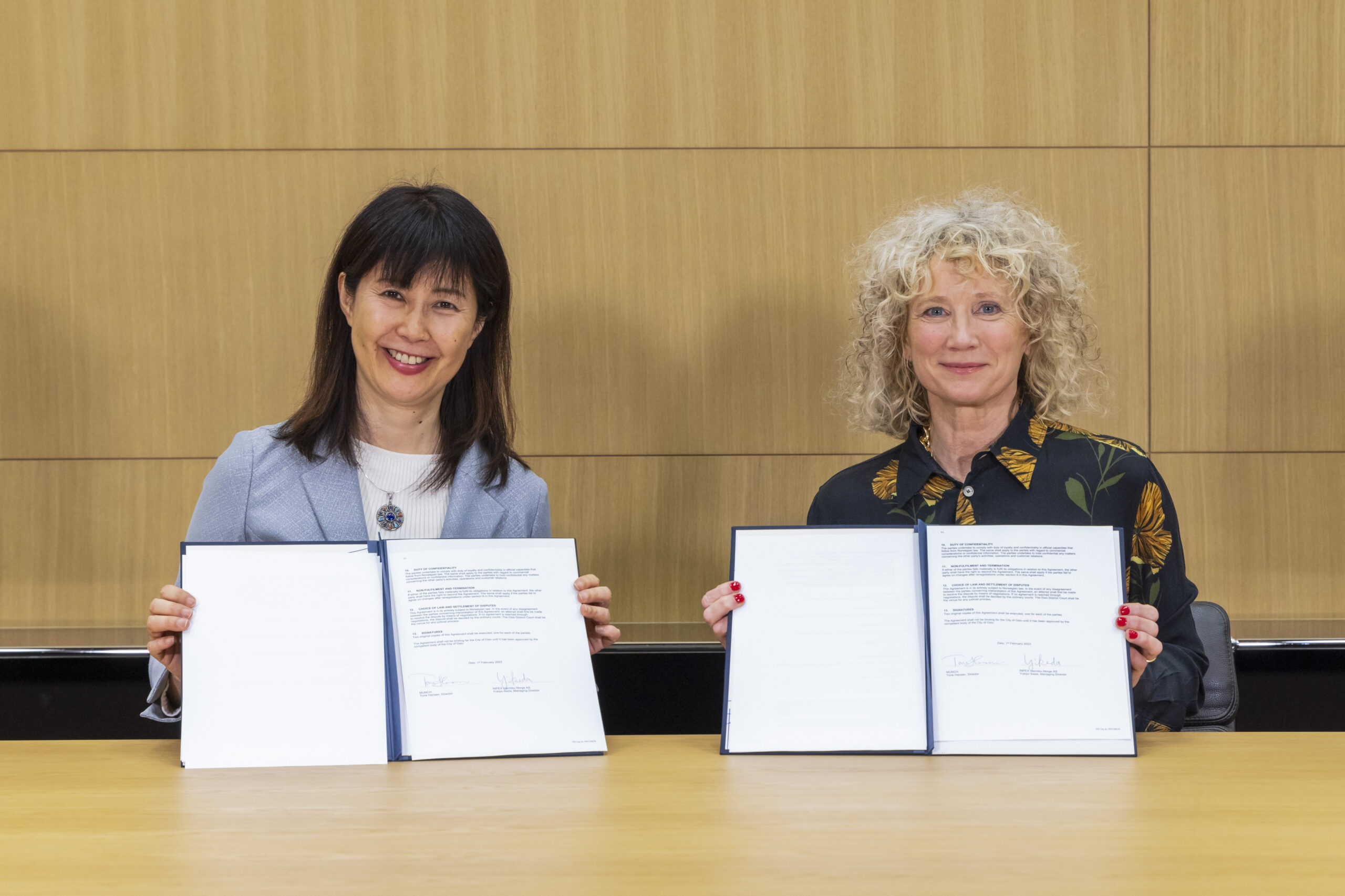 To smilende kvinner som holder opp en signert kontrakt